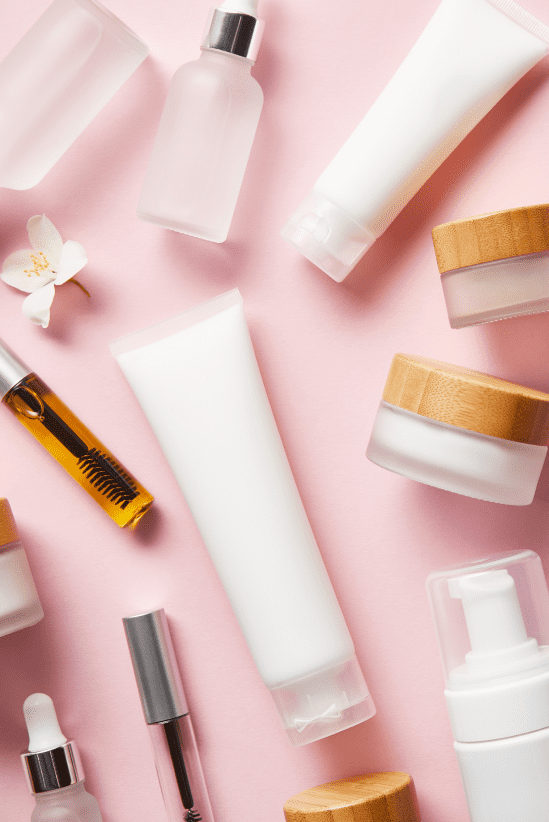 Skincare and cosmetic products in minimalist white packaging with wooden accents, arranged on a soft pink background.